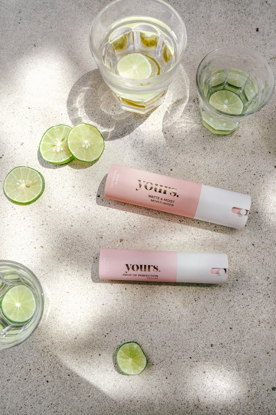 Skincare products with lime slices on a concrete surface.